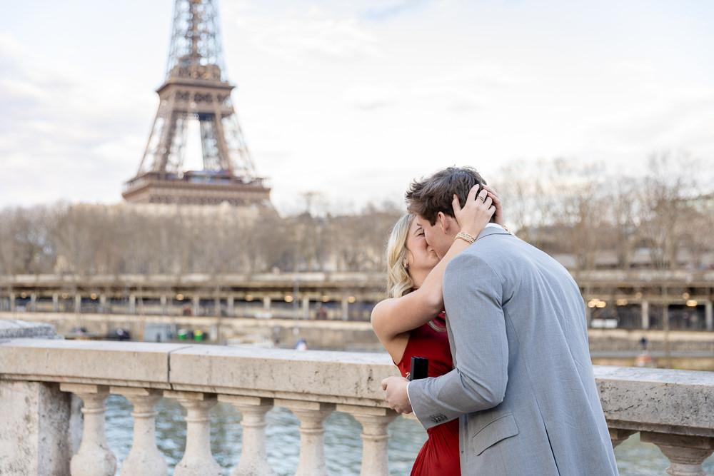 Couple kissing after she said yes, ring box still in hand, with the Eiffel Tower and the Seine behind them, by proposal photographer Lena