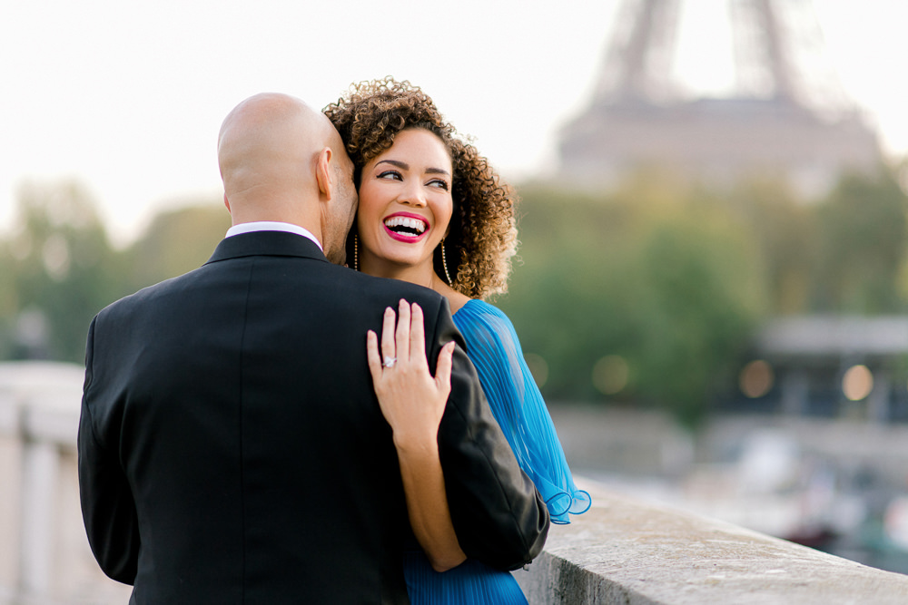 Woman in blue laughs over her partner's shoulder at sunrise, Eiffel Tower soft behind