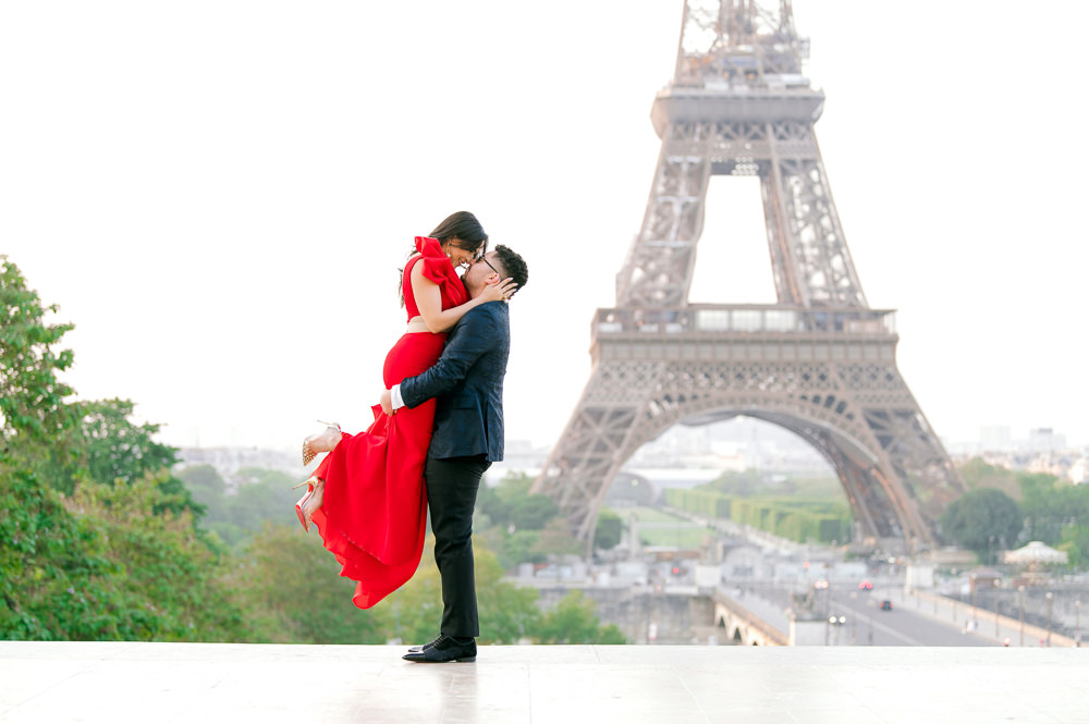 Man lifts his partner in a red gown for a kiss at Trocadéro, Eiffel Tower behind