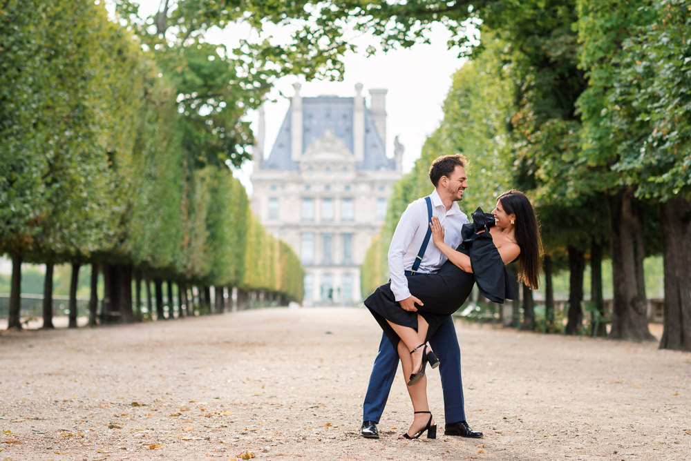 Man dips his partner in a tree-lined Tuileries alley, the Louvre behind them