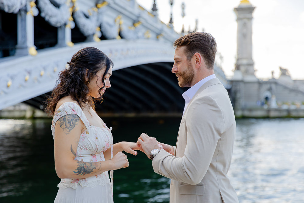 He slips the engagement ring on her finger beside Pont Alexandre III after a surprise proposal in Paris