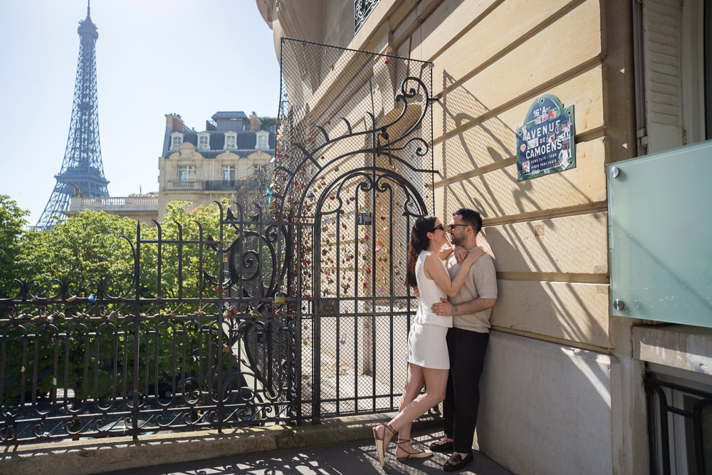 Couple kissing under the Avenue de Camoens street sign with the Eiffel Tower behind them after their surprise proposal in Paris