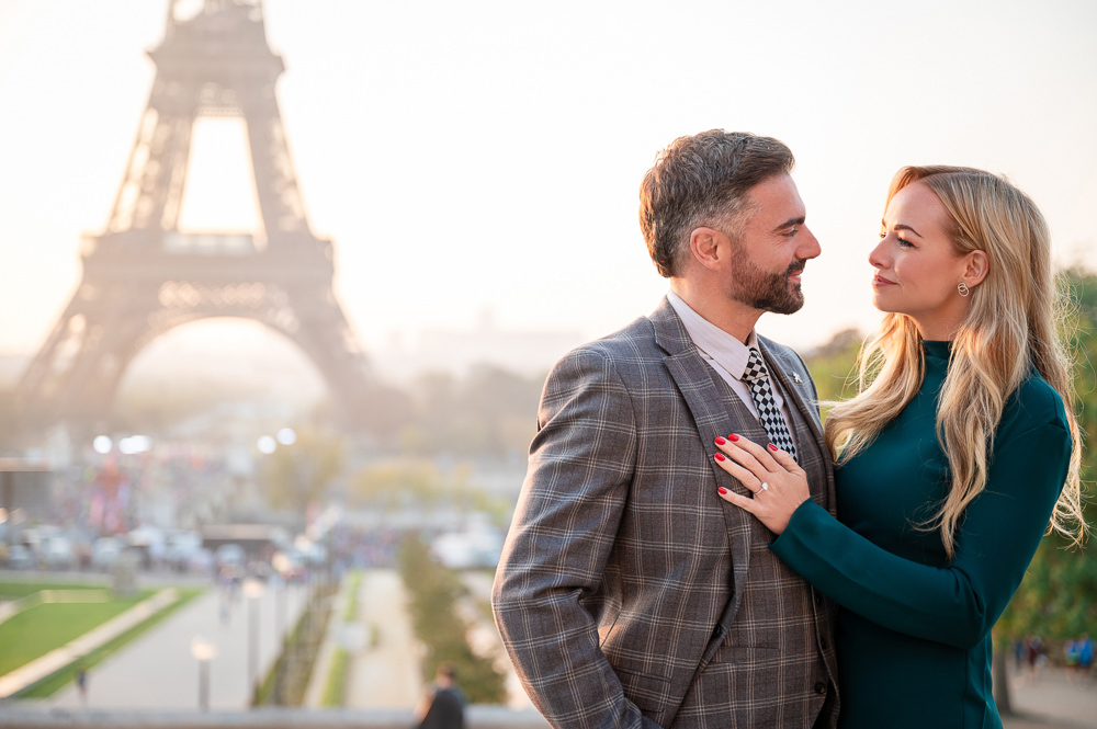 Engaged couple smiling at each other at Trocadéro at sunrise, her hand with the ring resting on his chest, Eiffel Tower in the background